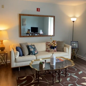 A fully furnished living room with a couch, rug, table, lamps, and a mirror.