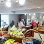 Two resident women operating the country store while one woman buys some items.